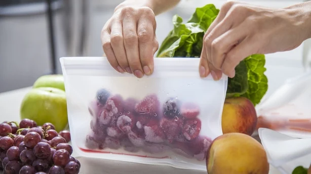 Una joven madre pone frambuesas congeladas en una bolsa transparente para guardar alimentos. 