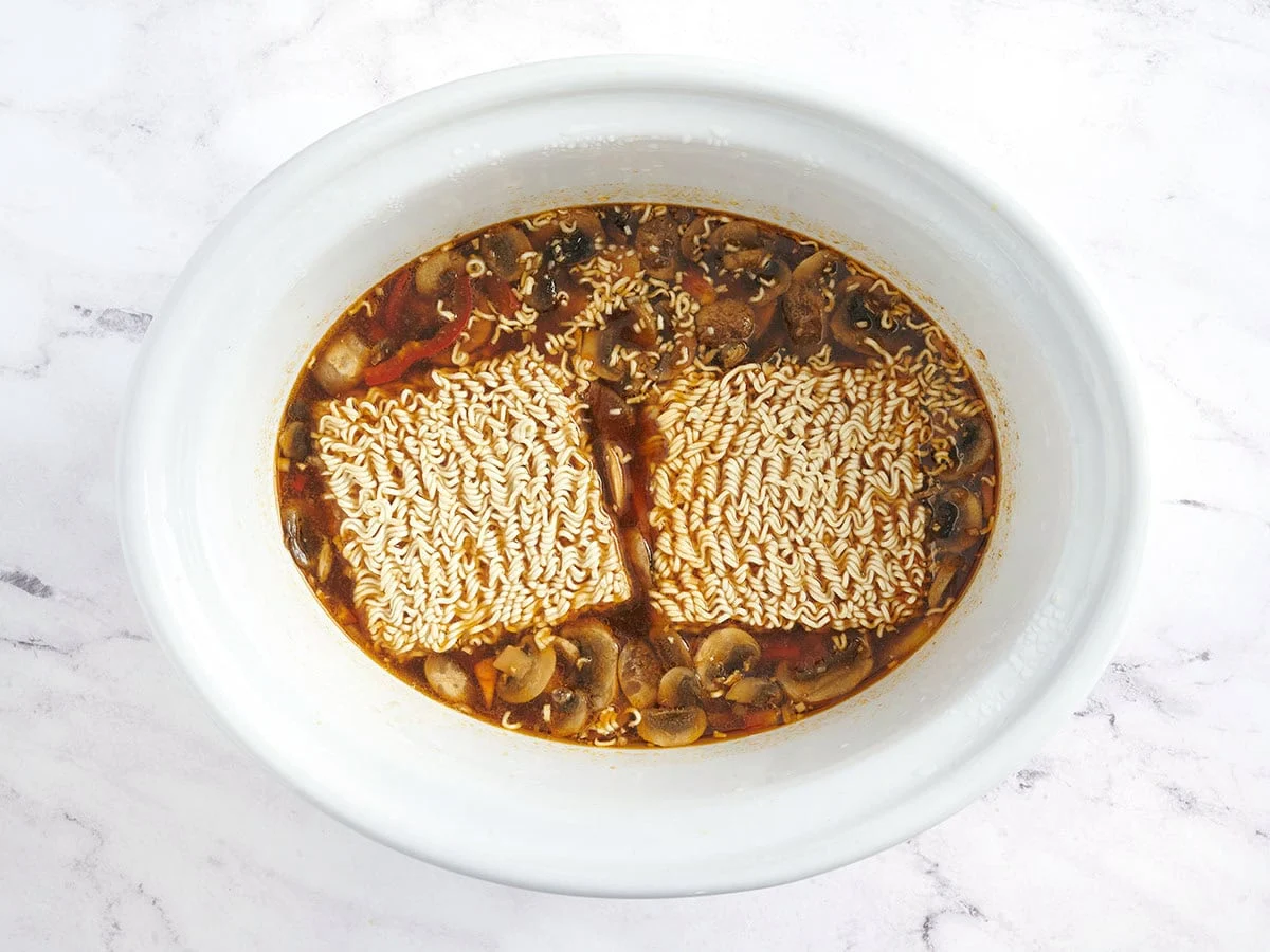 Fideos agregados a una olla eléctrica para hacer ramen de pollo y verduras en olla de cocción lenta.