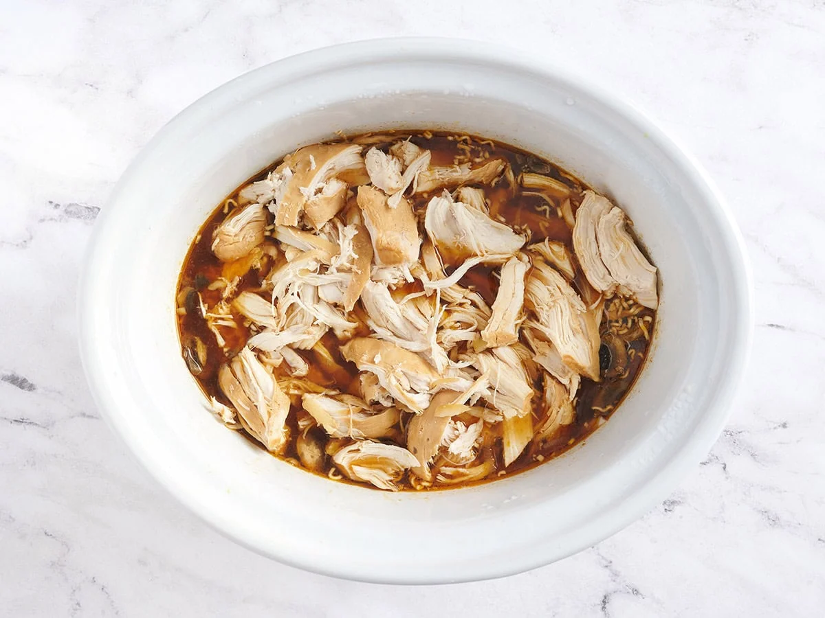 Pollo desmenuzado agregado nuevamente al caldo para hacer ramen en olla de cocción lenta.