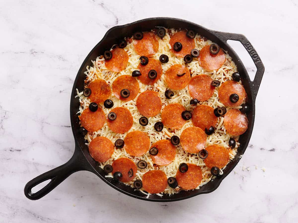 Pepperoni y aceitunas agregadas a una cazuela de pizza en una sartén.