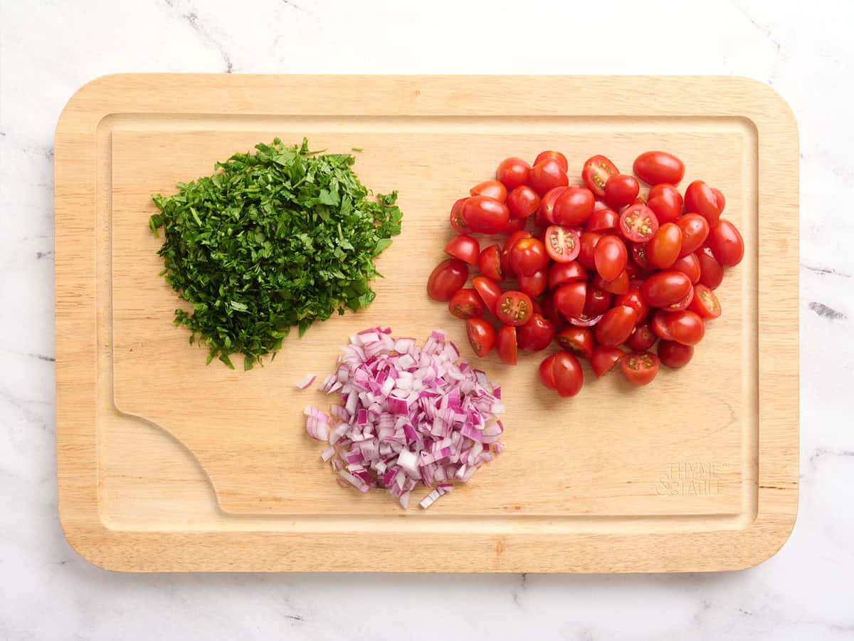 Tomates picados, perejil y cebolla morada sobre una tabla para cortar.