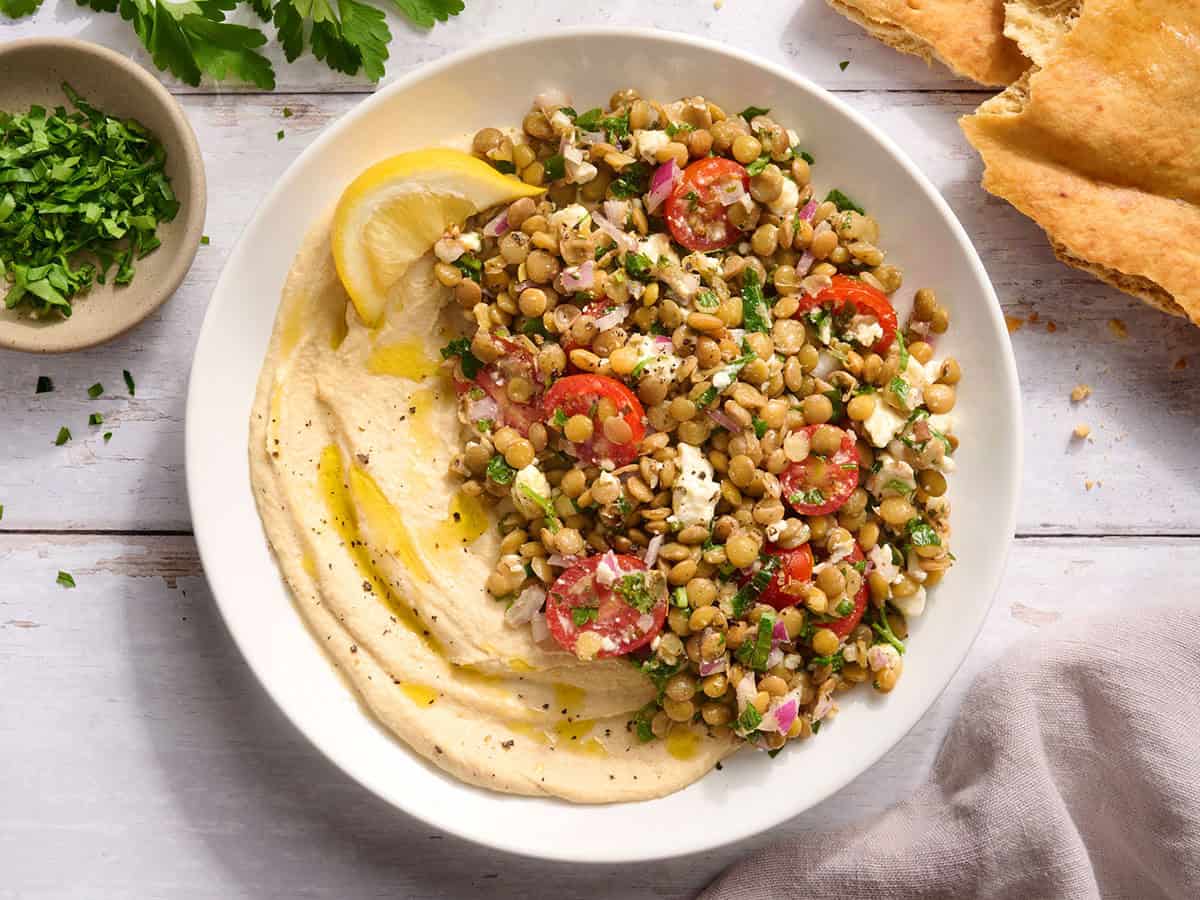 Un bol de hummus con ensalada de lentejas y una rodajita de limón.