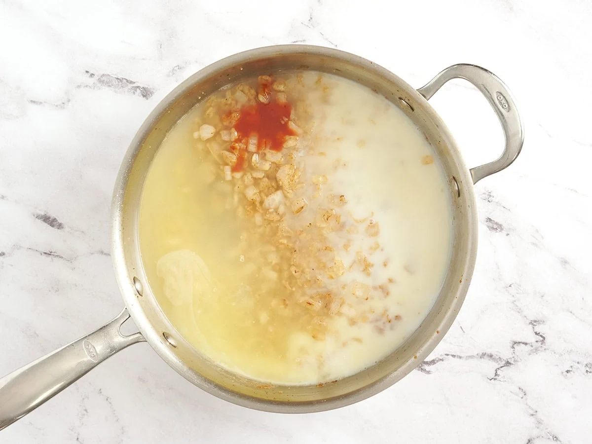Se agrega caldo de pollo, leche y salsa picante a una sartén con cebolla.