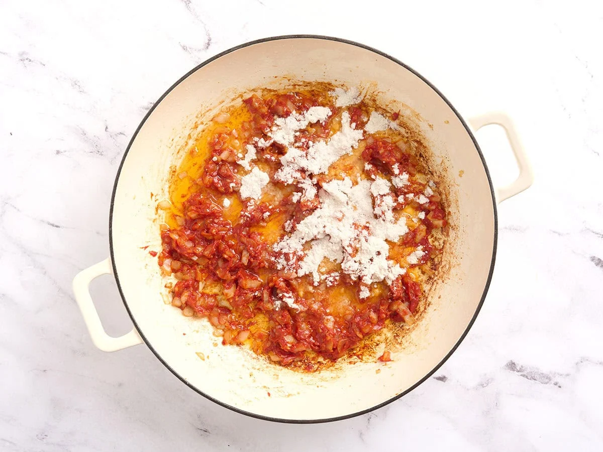 Se agrega harina a una sartén con cebolla y tomate para hacer un roux.