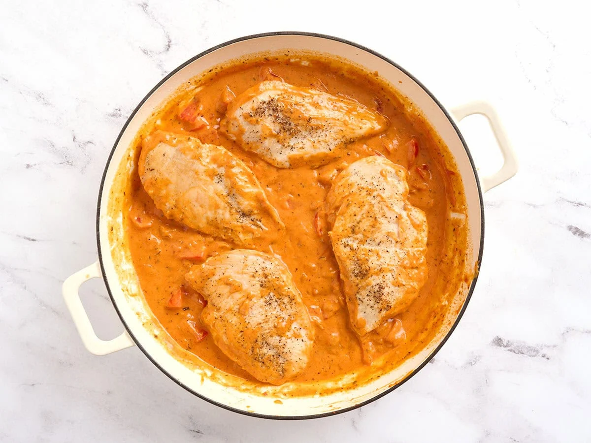 Pollo añadido a una sartén con salsa cremosa de tomate.