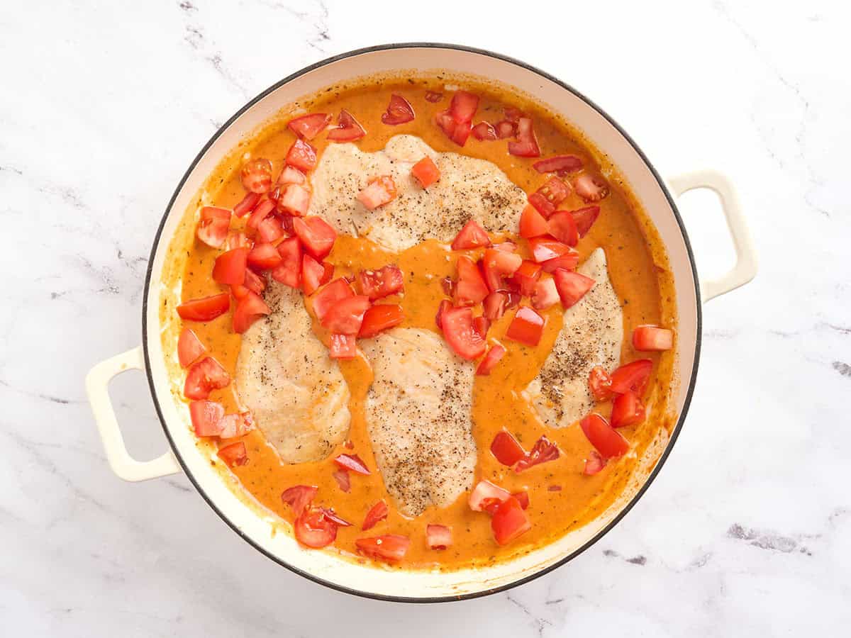 Tomates cortados en cubitos agregados a una sartén de pollo con tomate cremoso.