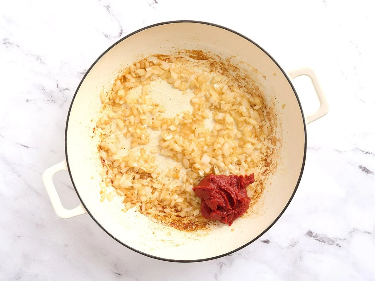 Pasta de tomate agregada a una sartén sobre cebollas y ajo salteados.