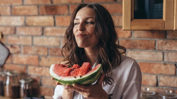 Mujer en casa comiendo sandía en la cocina.