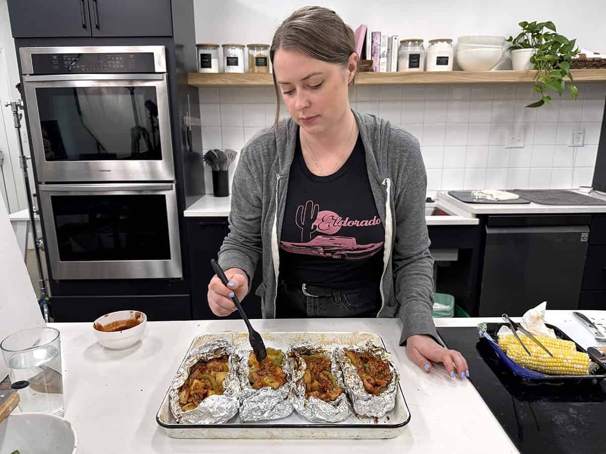Una mujer llenando paquetes de papel de aluminio de pollo BBQ en una cocina.