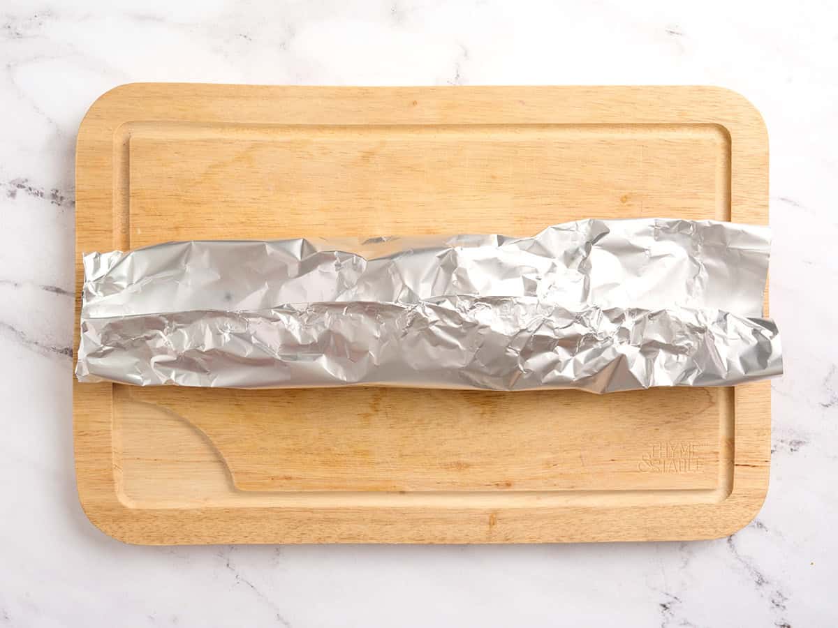 Un paquete de aluminio doblado por la mitad sobre una tabla de cortar de madera.