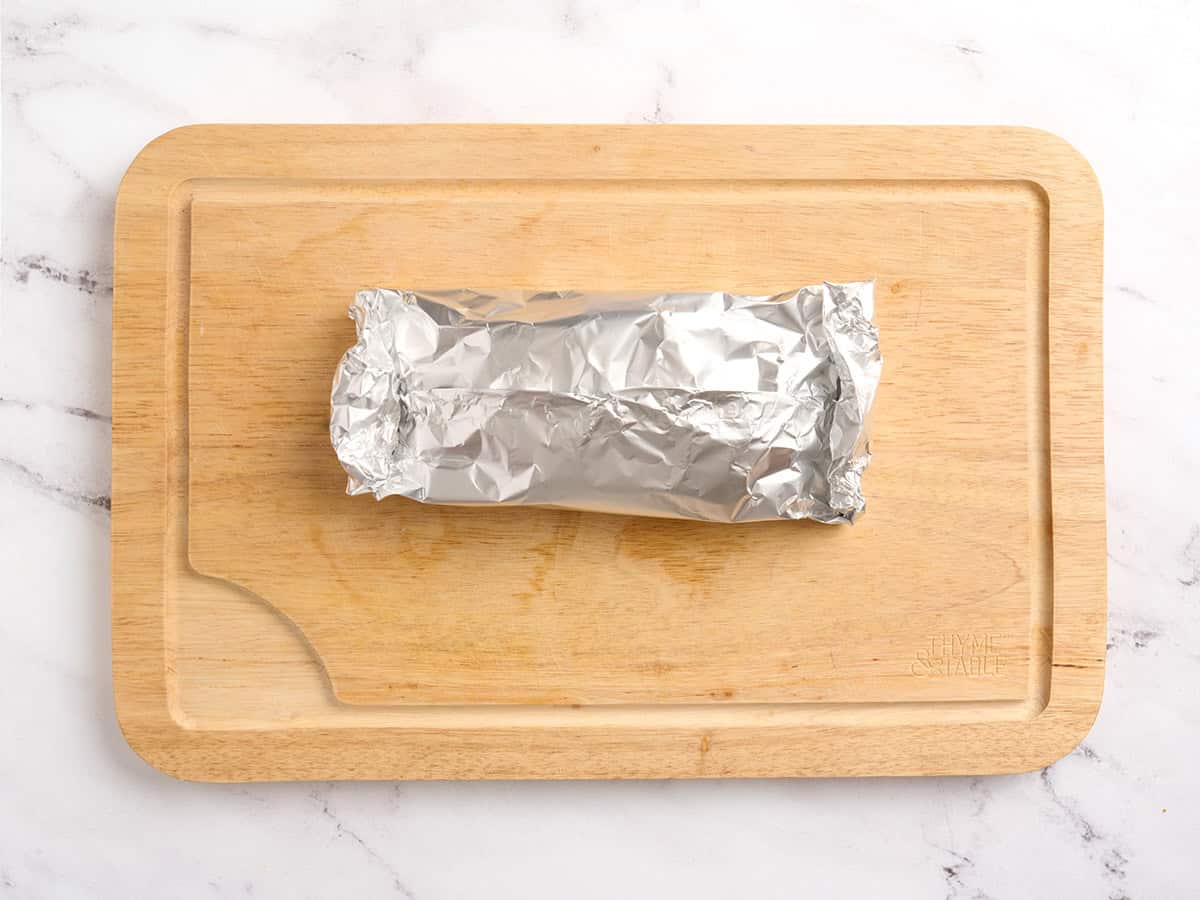 Un paquete de papel de aluminio doblado sobre una tabla de cortar de madera.