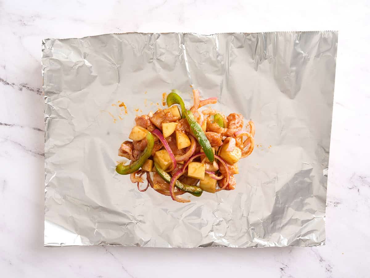 Pollo BBQ, patatas, pimientos y cebollas en una hoja de papel de aluminio.