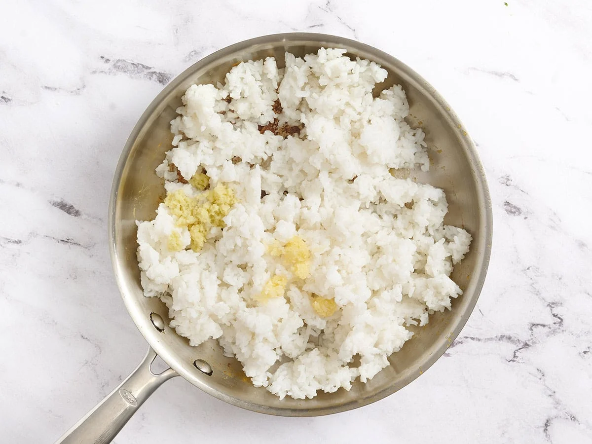 Jengibre y ajo añadidos a una sartén con arroz.