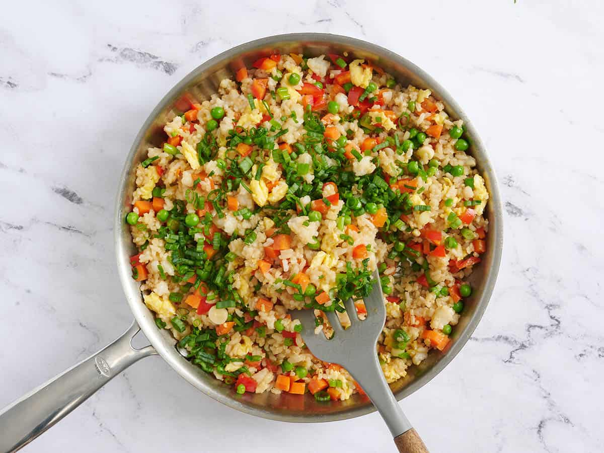 Las cebollas verdes se mezclan con arroz vegetal en una sartén.