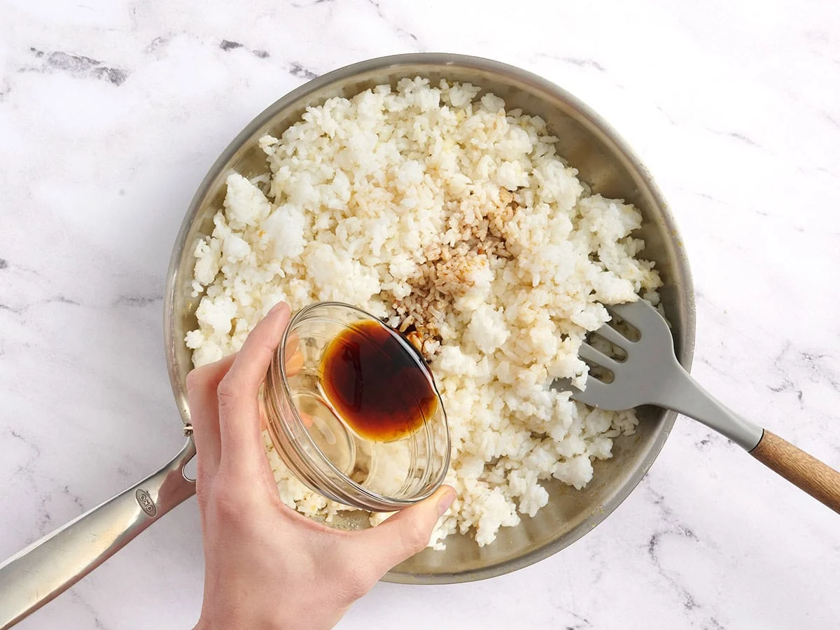 Se añade aceite de sésamo y salsa de soja a una sartén con arroz.