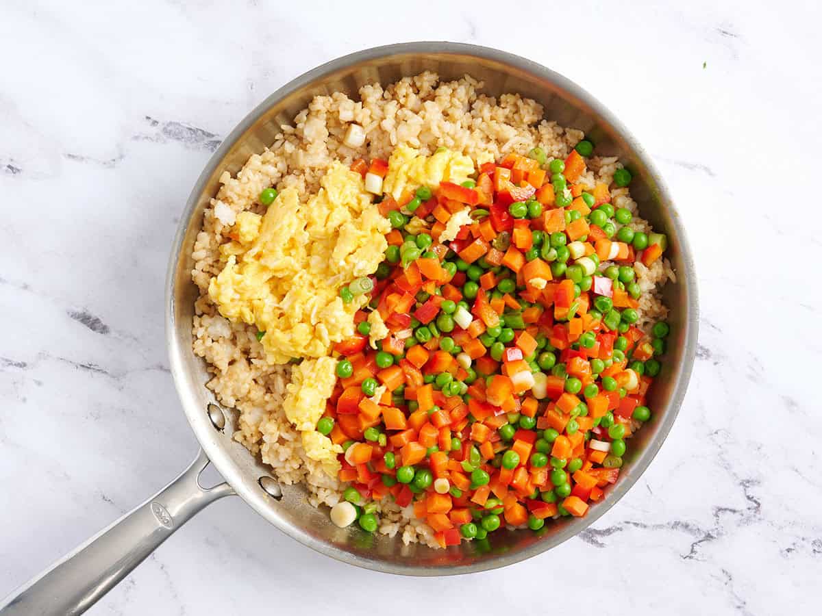 Huevos revueltos y verduras añadidos al arroz frito en una sartén.