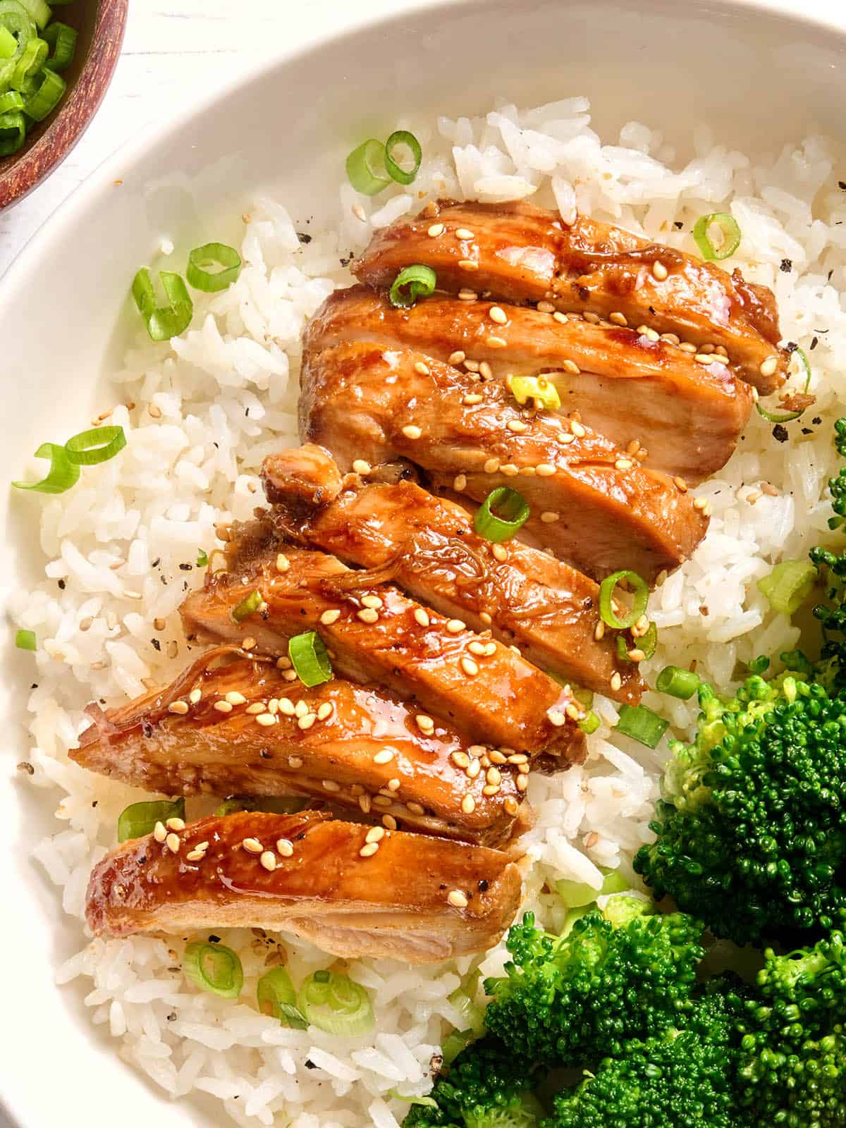 Vista aérea de pollo teriyaki en rodajas sobre una cama sobre arroz en un plato.