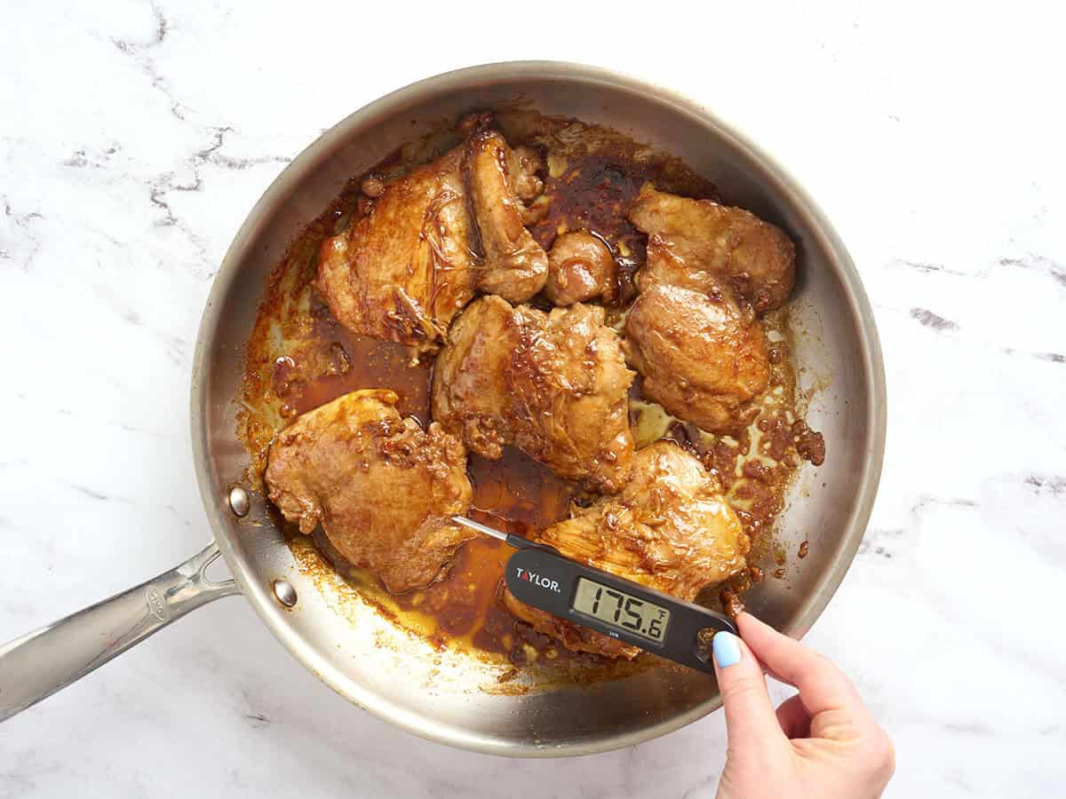 Se inserta un termómetro para carne en un muslo de pollo para comprobar la temperatura en la sartén.