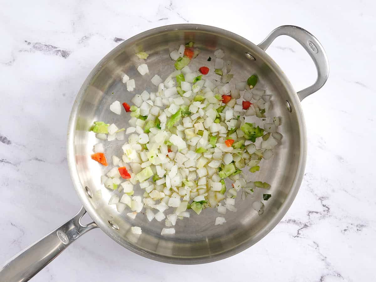 Pimientos y cebollas congelados cortados en cubitos en una sartén.