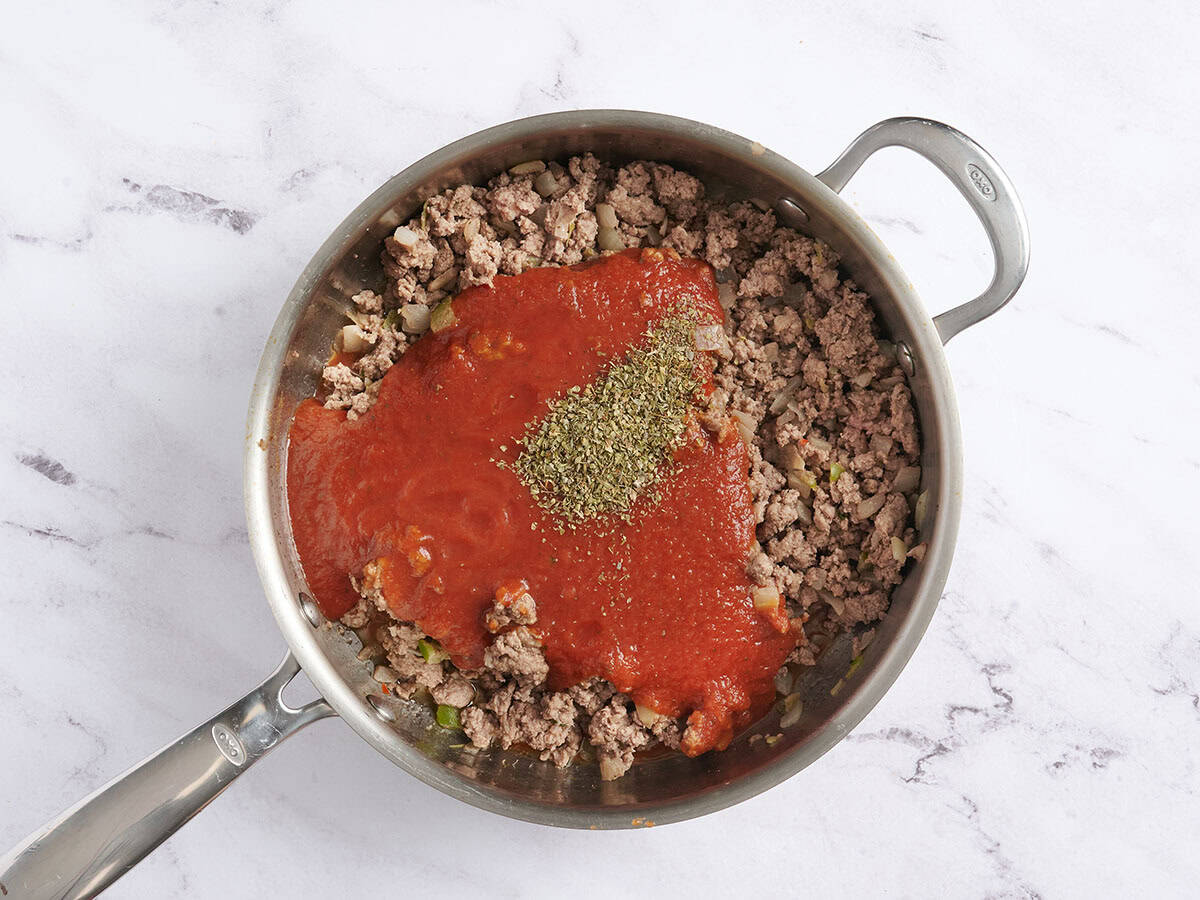 Salsa marinara agregada a una sartén con condimento italiano y carne molida dorada.