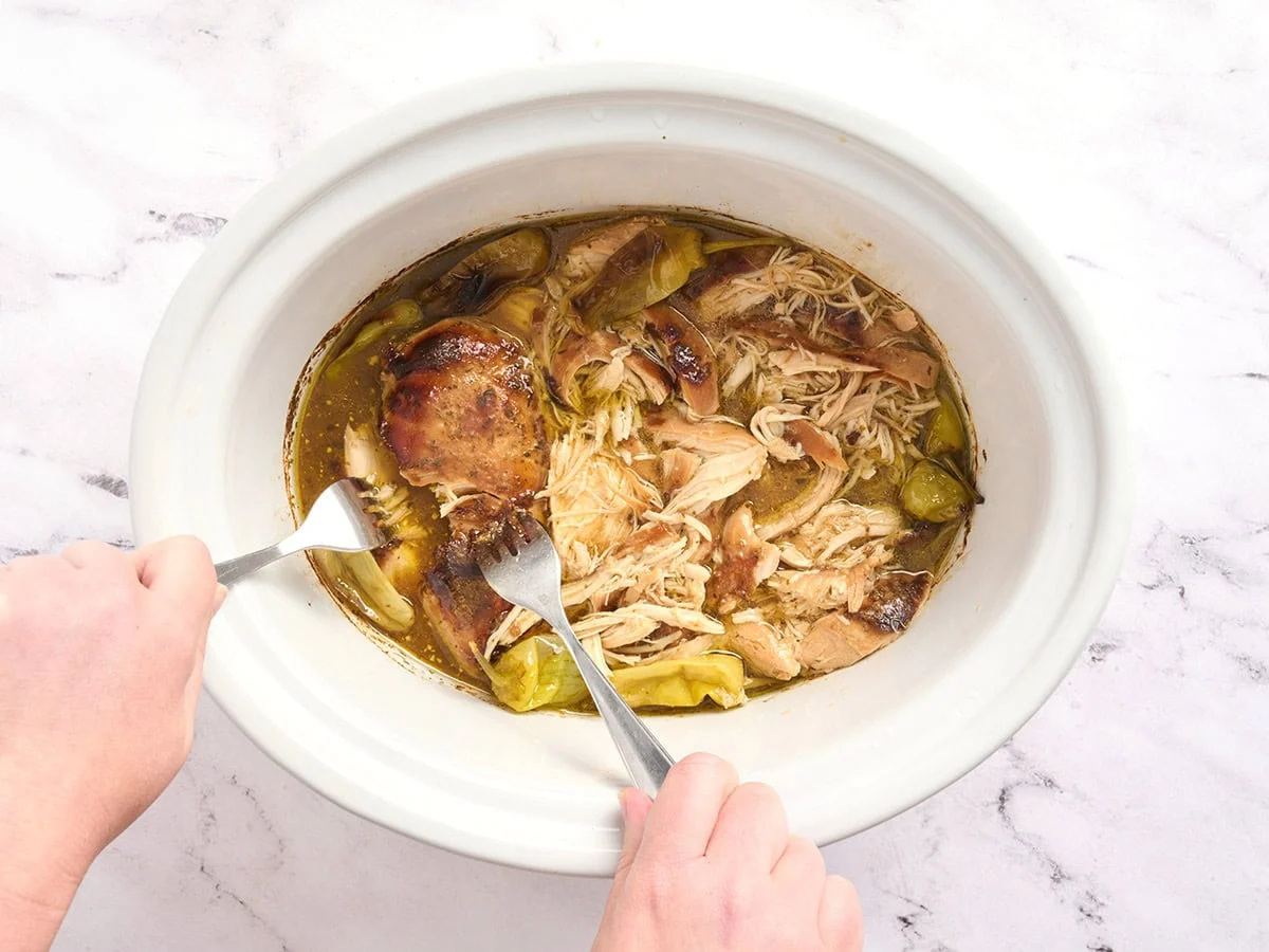 Con un tenedor, pollo Mississippi desmenuzado en una olla de cocción lenta.