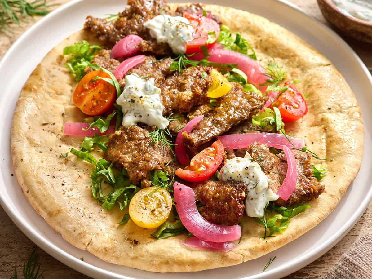 Vista lateral aérea de un doner kebab en sartén sobre una cuenta de pita con ensalada y salsa tzatziki.