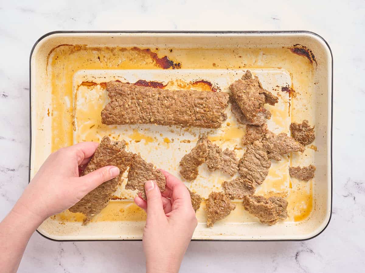 Manos triturando carne de kebab donner en trozos más pequeños.