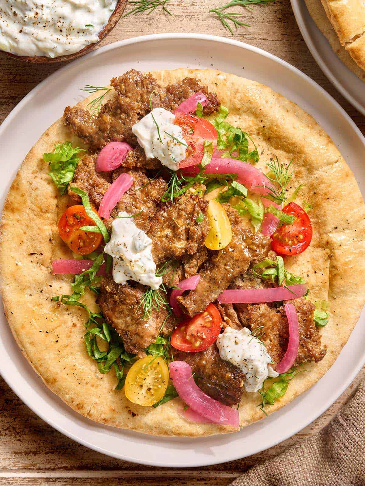 Vista aérea de un doner kebab en sartén sobre una cuenta de pita con ensalada y salsa tzatziki.