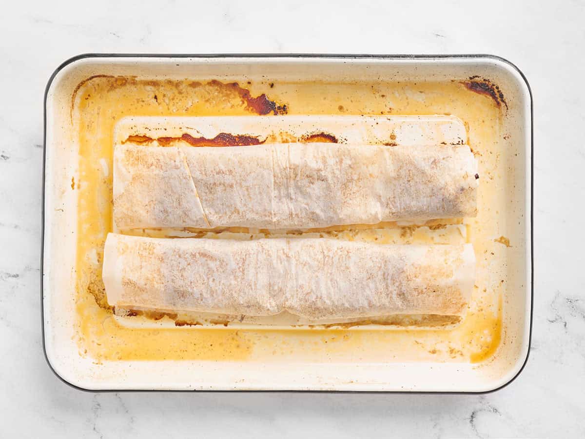 Carne molida cocida envuelta en papel pergamino en una bandeja para hornear.