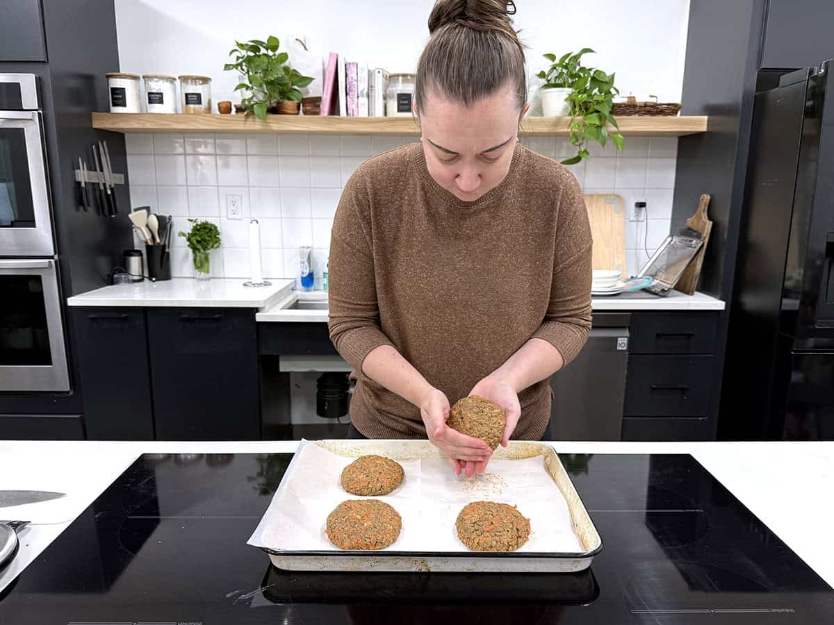 Una mujer dando forma a hamburguesas de lentejas en una cocina.