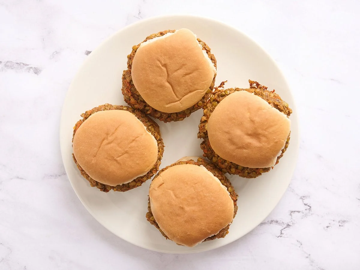 Vista aérea de cuatro hamburguesas de lentejas en panecillos de hamburguesa en un plato.