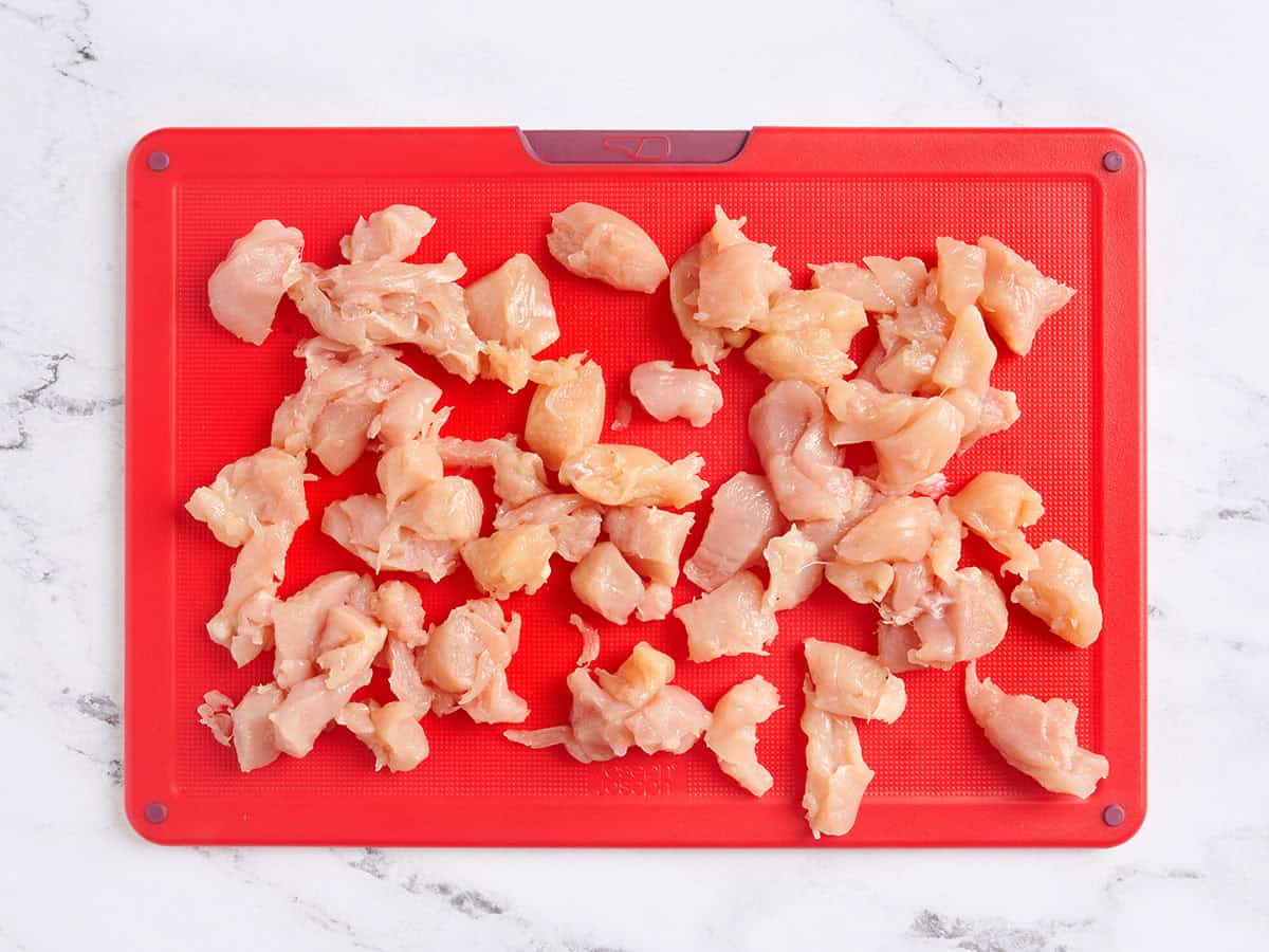 Trozos de pollo cortados en trozos pequeños sobre una tabla de cortar.