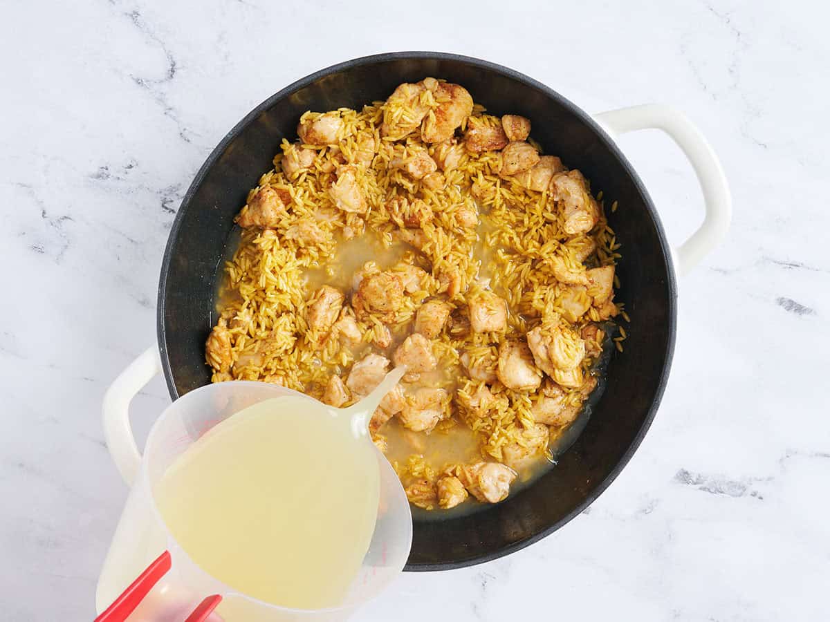 Se vierte caldo en una sartén con pollo cocido y orzo tostado.