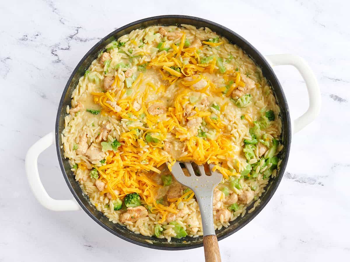 Se mezcla queso cheddar rallado en una cazuela de pollo y brócoli.