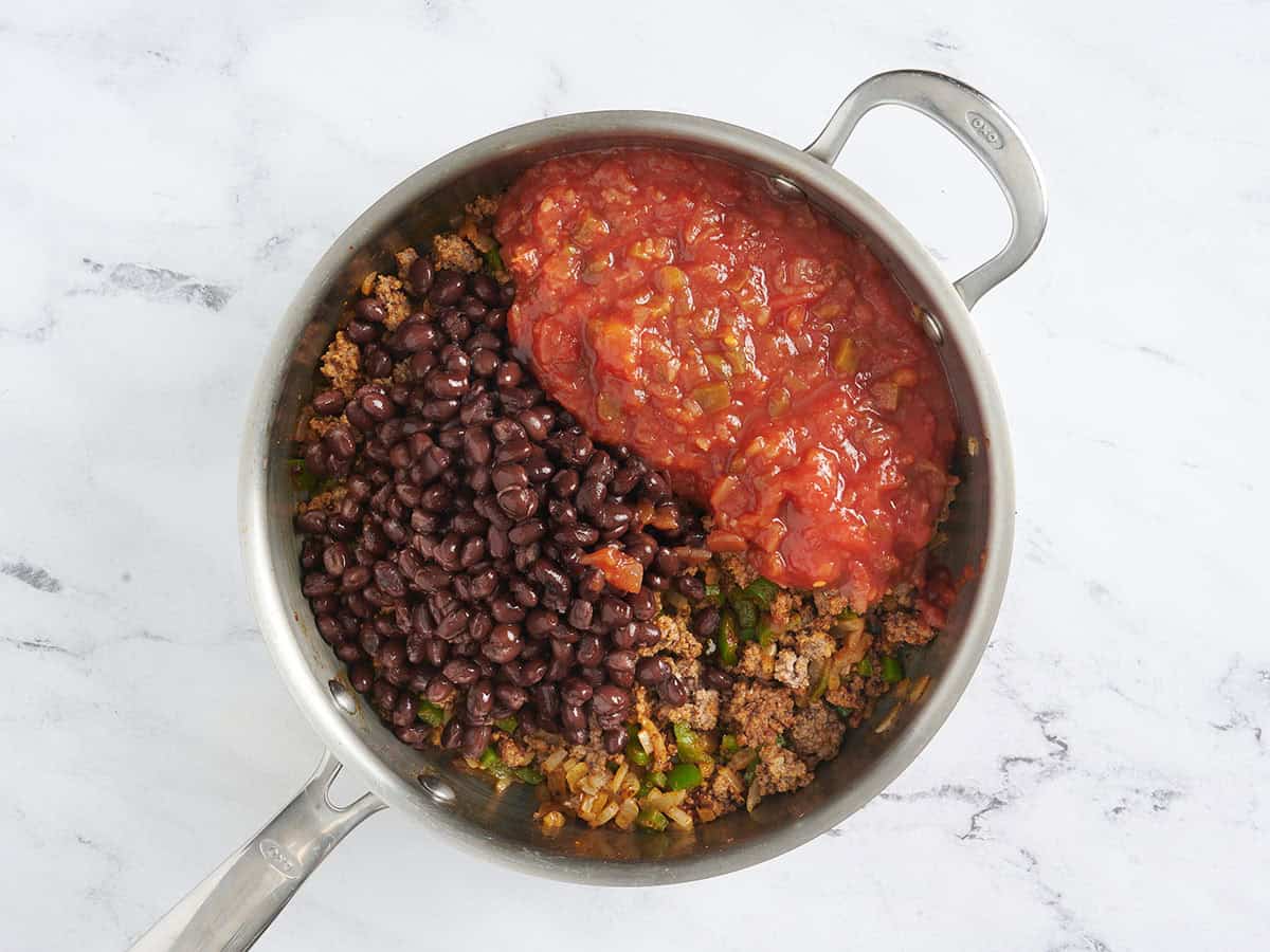 Frijoles negros y salsa agregados a una sartén con carne molida dorada.
