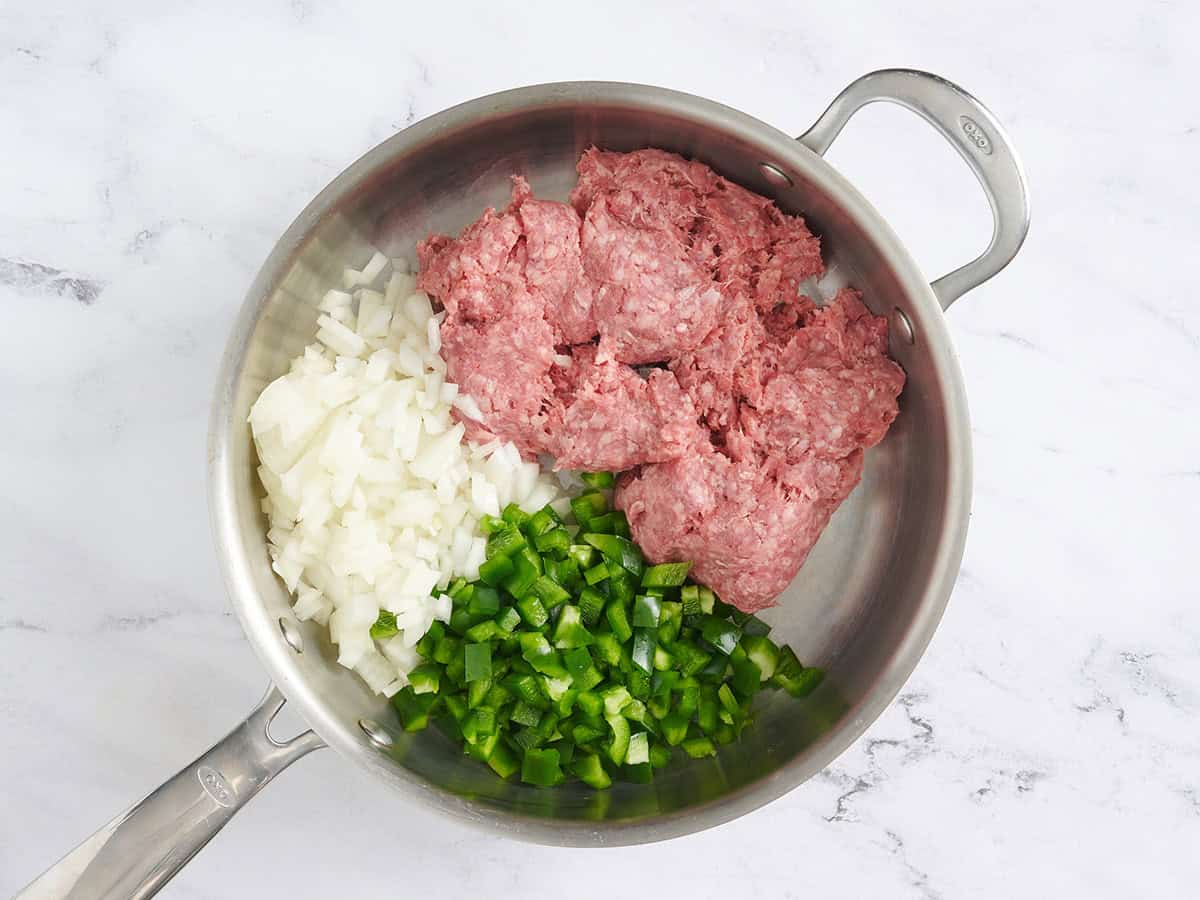 Carne molida, cebolla picada y pimiento verde picado en una sartén.
