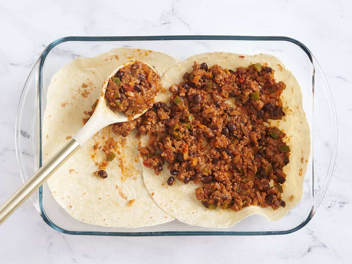 Tortillas en capas en una fuente para horno con carne para tacos encima.