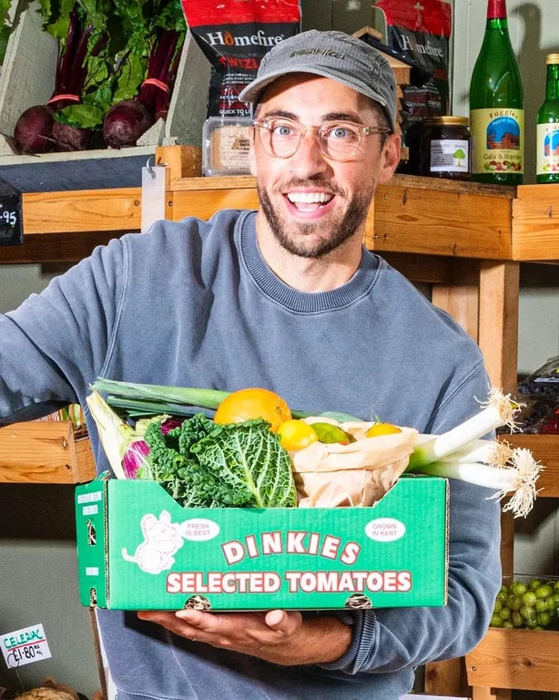 Makin sosteniendo una caja de verduras.
