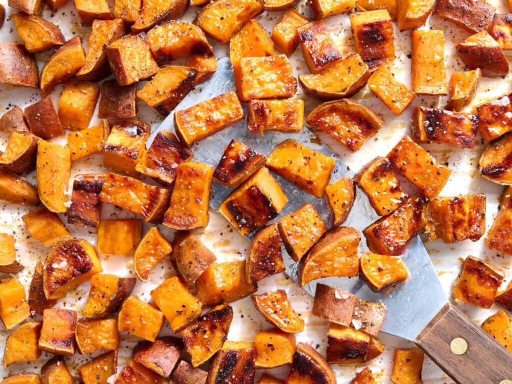 Overhead view roasted sweet potatoes with a metal spatula scooping some up.