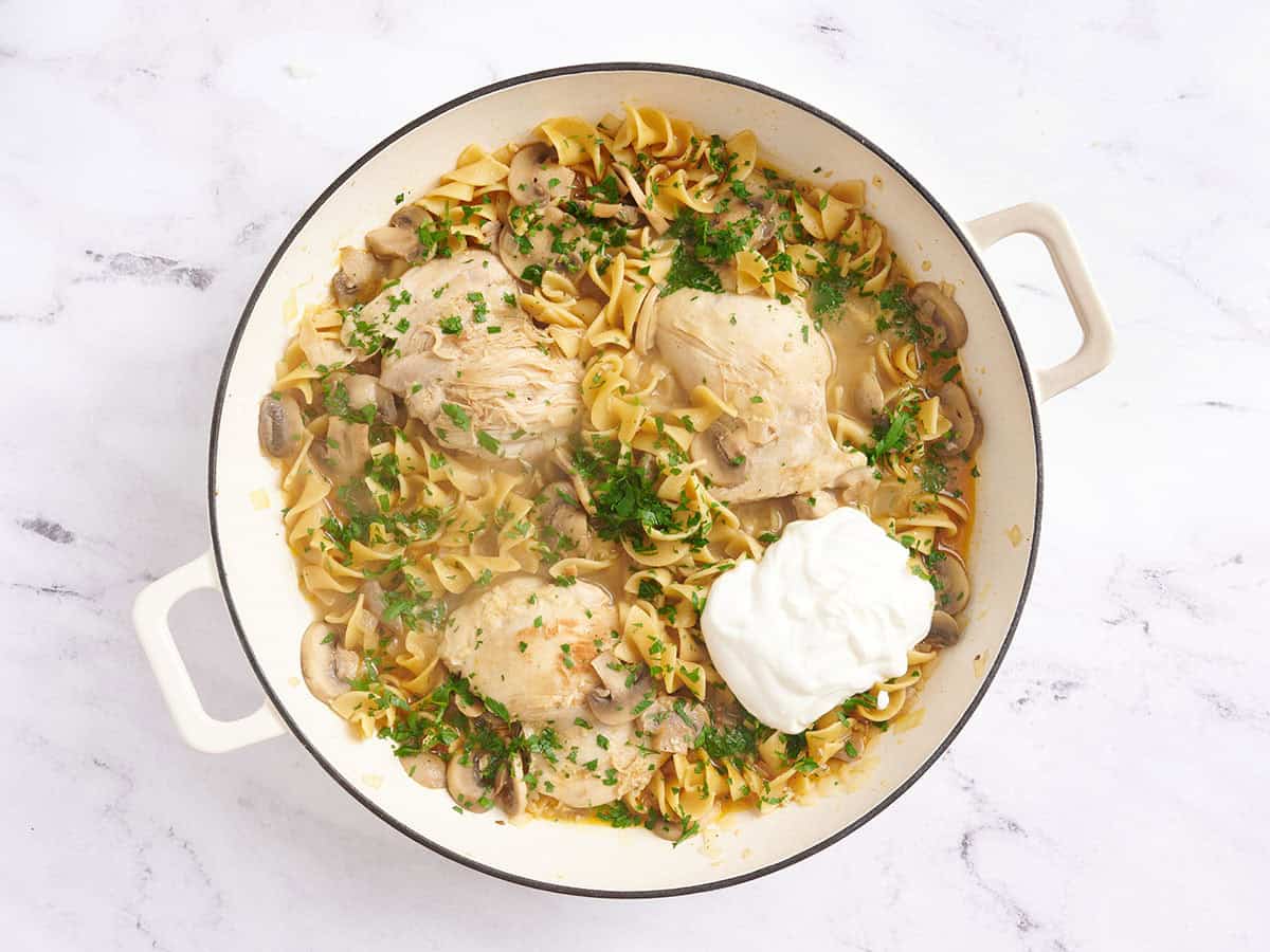 Crema agria y perejil fresco añadidos a una sartén con pollo stroganoff.