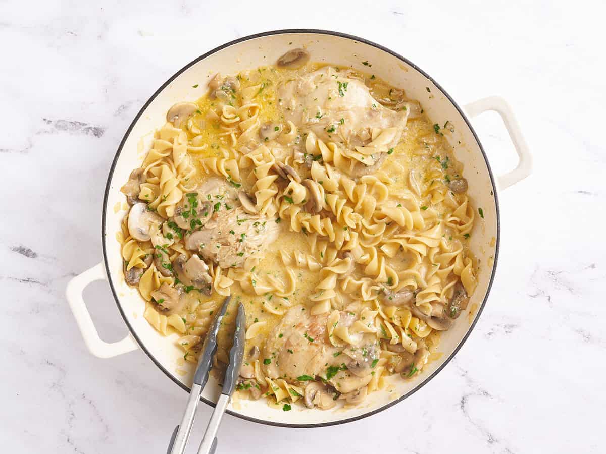 Stroganoff de pollo en una sartén con pinzas de cocina.