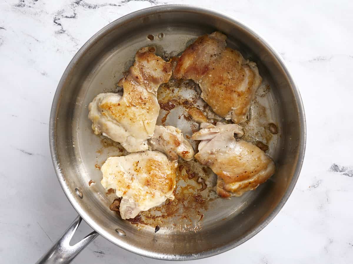 Muslos de pollo dorados en una sartén profunda.