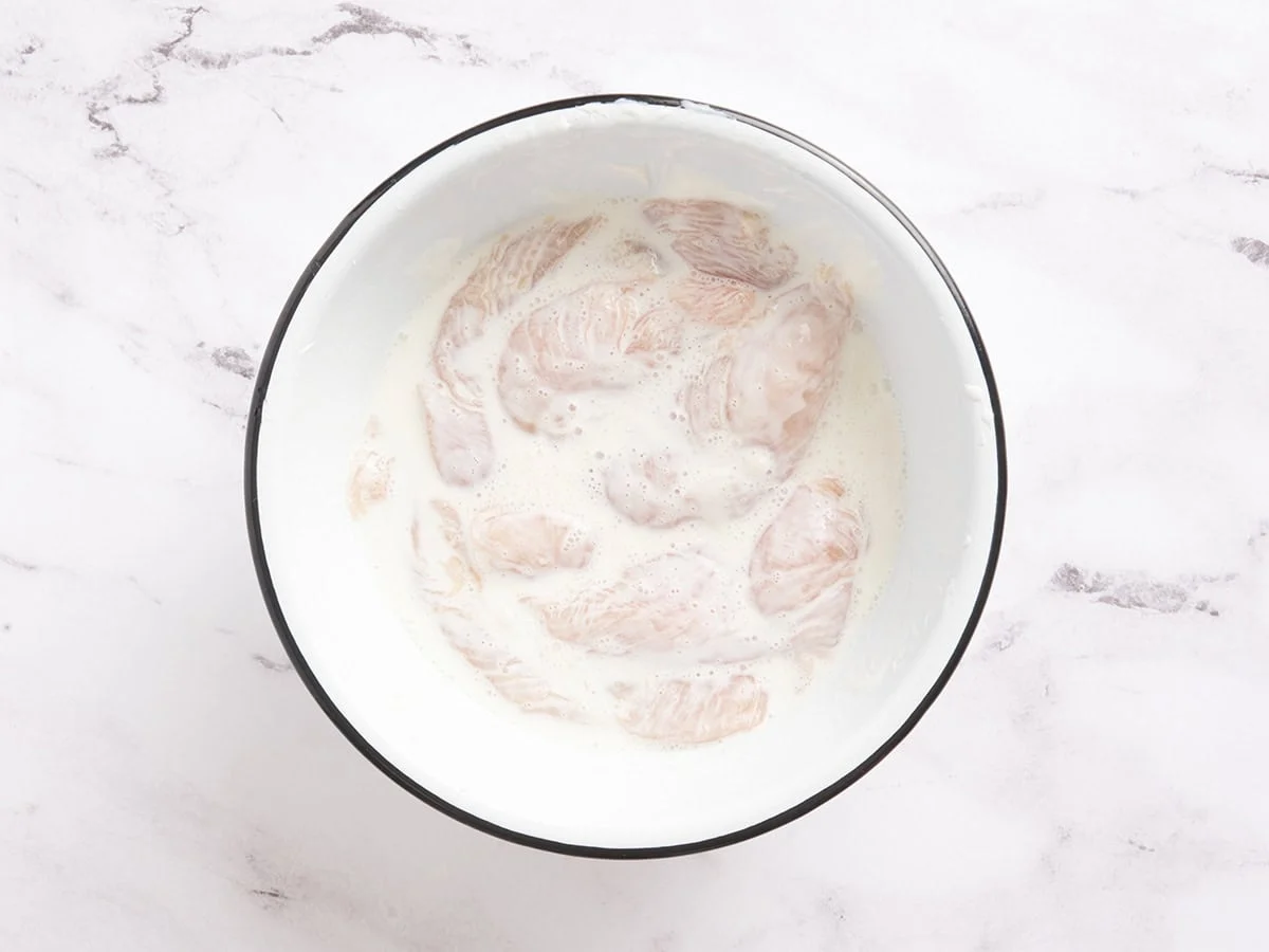 Trozos de pollo en un bol con yogur y agua.