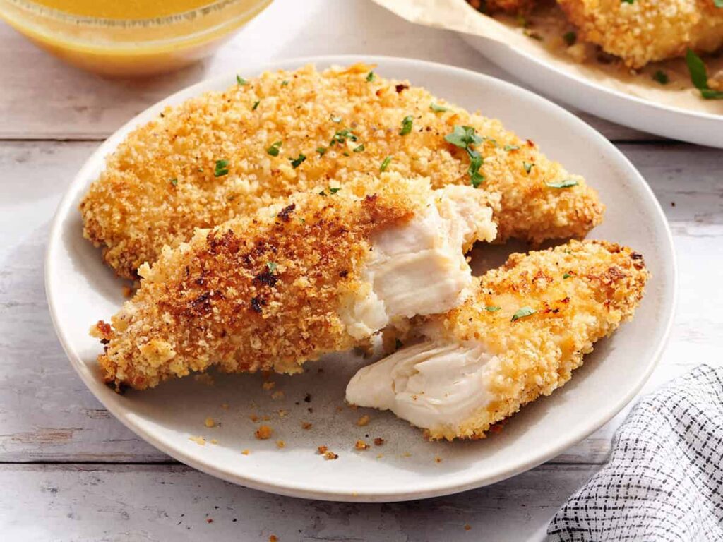 Side view of chicken tenders on a plate, with one of them split in half.