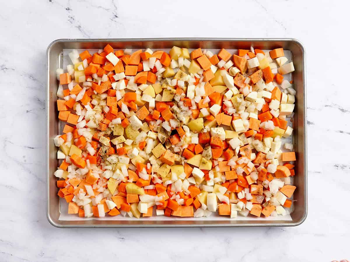 Verduras de raíz cortadas en cubitos en una bandeja para hornear cubiertas con condimentos.