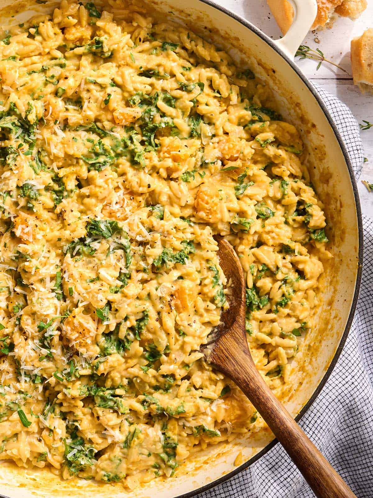 Vista aérea de cerca de una sartén de orzo cremoso de calabaza con una cuchara de madera.