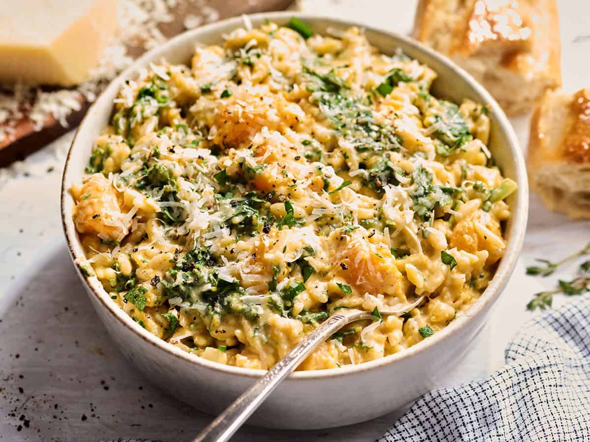 Vista lateral de un plato de orzo cremoso de calabaza con queso parmesano rallado y un tenedor.