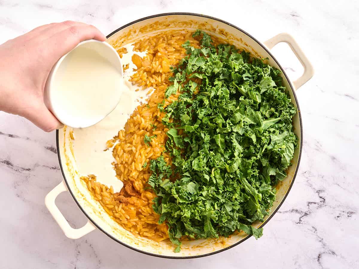 Orzo de calabaza en una sartén con col rizada fresca y crema.