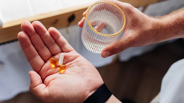 Primer plano de una persona que se prepara para tomar suplementos vitamínicos con un vaso de agua en casa. Bienestar diario, rutina de atención médica y concepto de autocuidado.