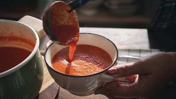 Una persona sirviendo un plato de sopa de tomate.